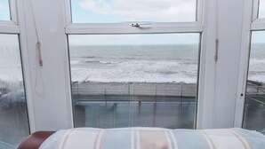 A room with a large window overlooking the sea, a bed with a striped blanket, and a view of the beach. - The View (Criccieth)