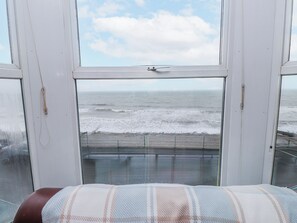 Ein Zimmer mit großem Fenster und Blick auf das Meer, einem Bett mit gestreifter Decke und einer Aussicht auf den Strand.