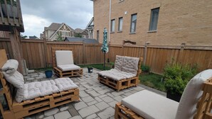 Een terras buiten met houten meubels, waaronder een bank en stoelen, gelegen op een geplaveid terras.