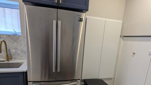 Een keuken met een roestvrijstalen koelkast, een spoelbak, kastjes en een prullenbak.