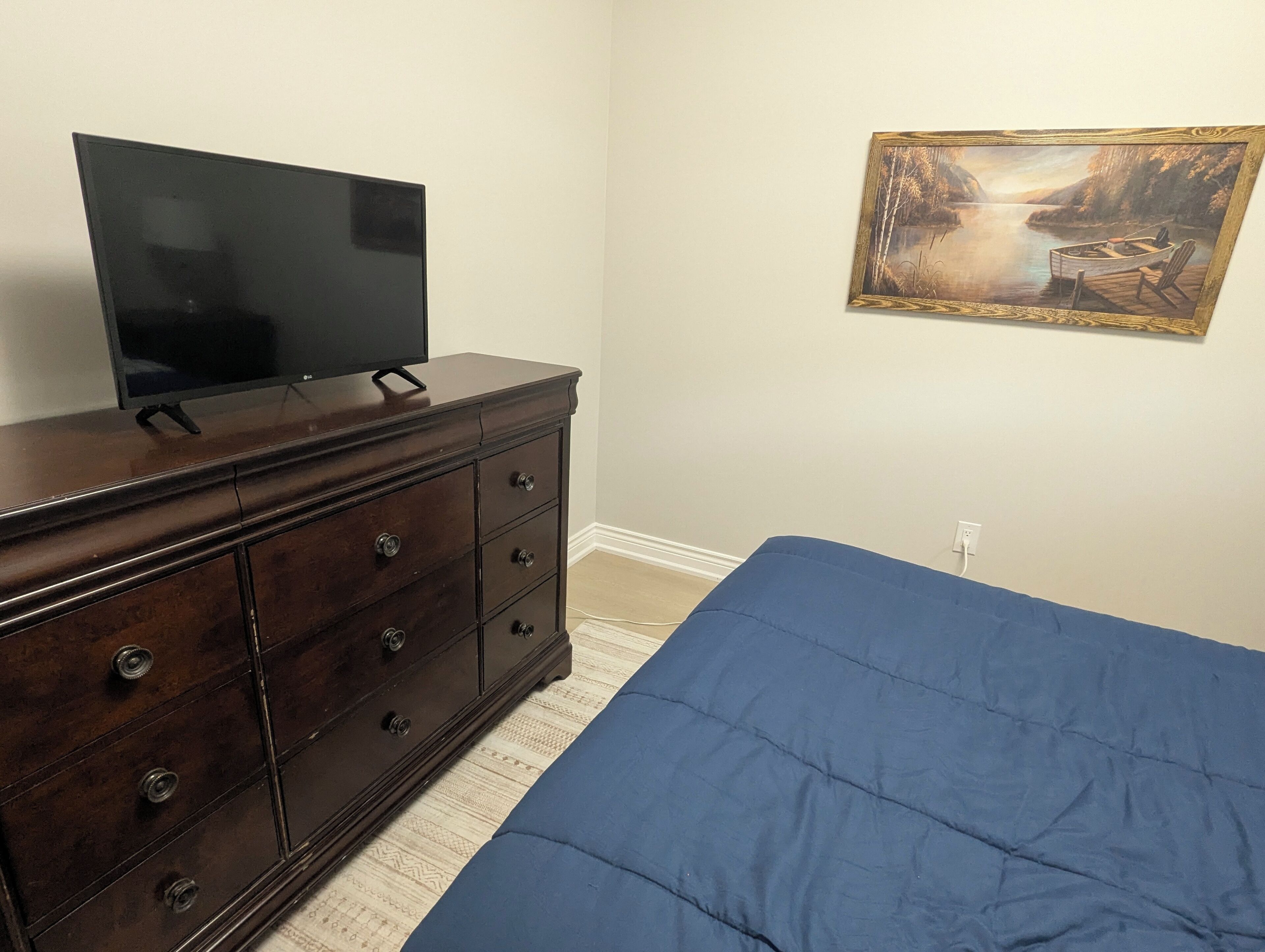 Une chambre à coucher avec un lit, une commode, un téléviseur posé sur la commode et un tableau accroché au mur.