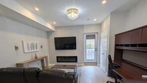 Een moderne woonkamer met een leren bank, een flatscreen televisie, een open haard en een houten bureau.
