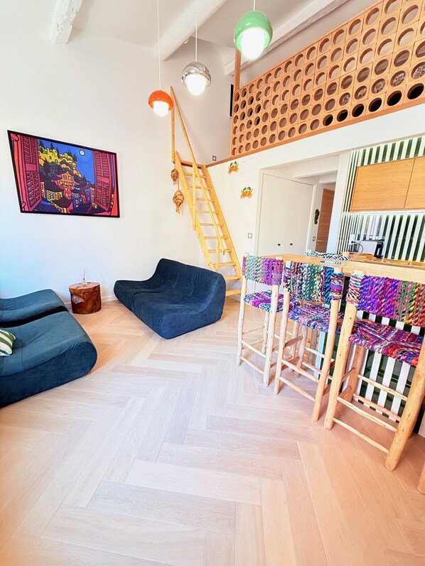A modern living room with a herringbone floor, a blue sofa, a wooden ladder, and a colorful woven chair.