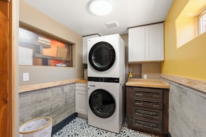 A compact laundry room with a stacked washer and dryer, wooden cabinets, and patterned floor tiles. - Luxury Point Loma Stay - Central, Coastal & Unique (San Diego)