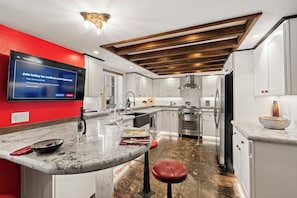 A modern kitchen with a marble countertop, stainless steel appliances, and a red accent wall. - Luxury Point Loma Stay - Central, Coastal & Unique (San Diego)