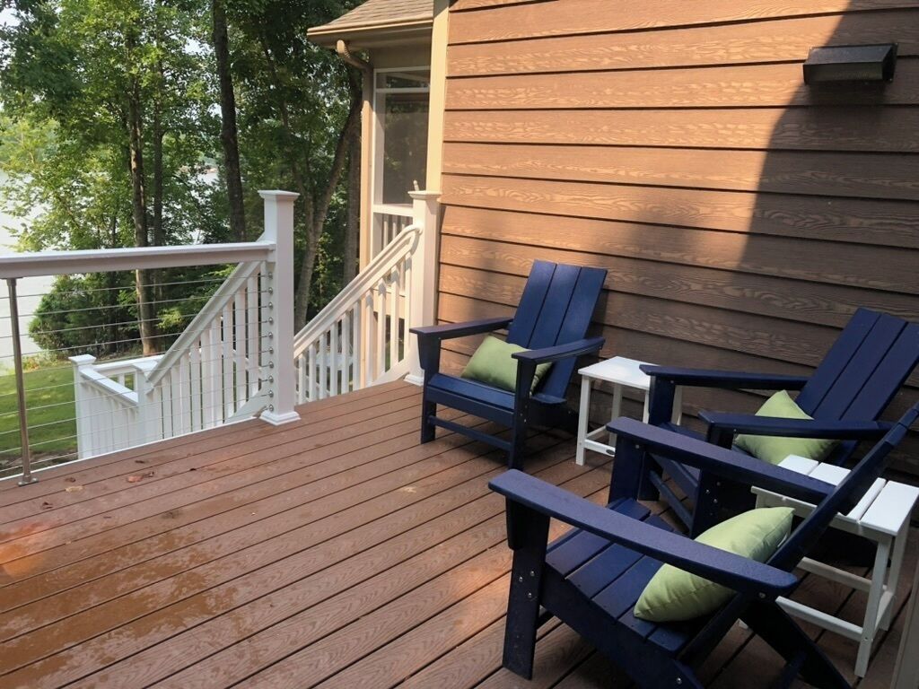 Une terrasse en bois avec deux chaises bleues et une petite table, une balustrade blanche et une maison en arrière-plan.