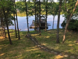 Järven rannalla sijaitseva mökki, jolle johtaa kivipolku, ja sen ympärillä on puita.