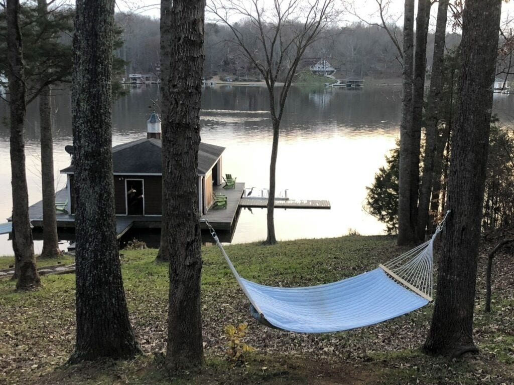 A lakeside cabin with a hammock, dock, and docked boats.