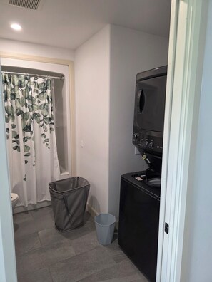 A small bathroom with a shower curtain, a trash bin, and a washing machine.