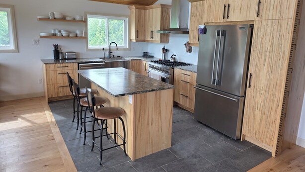 Una cocina moderna con armarios de madera, una isla central con taburetes de bar, un refrigerador de acero inoxidable y un ventanal que proporciona luz natural.