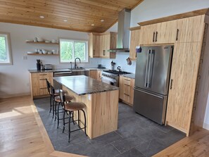 Una cucina moderna con mobili in legno, un'isola centrale con sgabelli da bar, un frigorifero in acciaio inossidabile e una finestra che offre luce naturale.