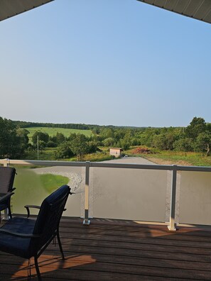 A covered outdoor area with a view of a green landscape, a small structure, and two chairs.