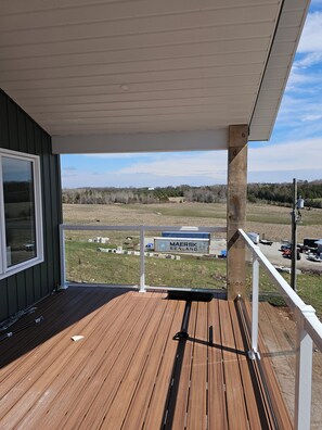 A wooden deck with a white railing, a clear view of a distant landscape, and a building with a sign reading 'MAERSK HIKING'.
