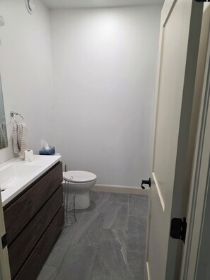 A bathroom with a white sink, dark wooden vanity, a toilet, and grey tiled flooring.
