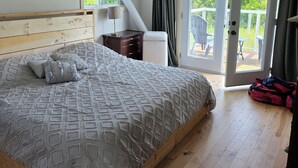 Un dormitorio con cama, ventilador de techo, mesita de noche, lámpara y vista a una terraza exterior por una puerta corrediza de vidrio.
