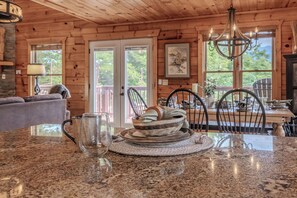 A wooden cabin interior with a dining table, chairs, a chandelier, and a view through the windows. - Summit Views | Hot Tub, Sauna, Fire Pit & Game Room, Near Gatlinburg (Gatlinburg)
