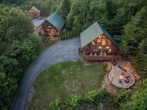 A log cabin with a curved driveway, a deck with outdoor seating, and a fire pit area. - Summit Views | Hot Tub, Sauna, Fire Pit & Game Room, Near Gatlinburg (Gatlinburg)