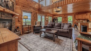 A spacious cabin interior with a fireplace, leather seating, a dining area, and a kitchen. - Summit Views | Hot Tub, Sauna, Fire Pit & Game Room, Near Gatlinburg (Gatlinburg)