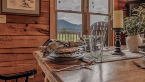 A wooden interior with a dining table set for two, a candle, and a view of mountains through a window. - Summit Views | Hot Tub, Sauna, Fire Pit & Game Room, Near Gatlinburg (Gatlinburg)