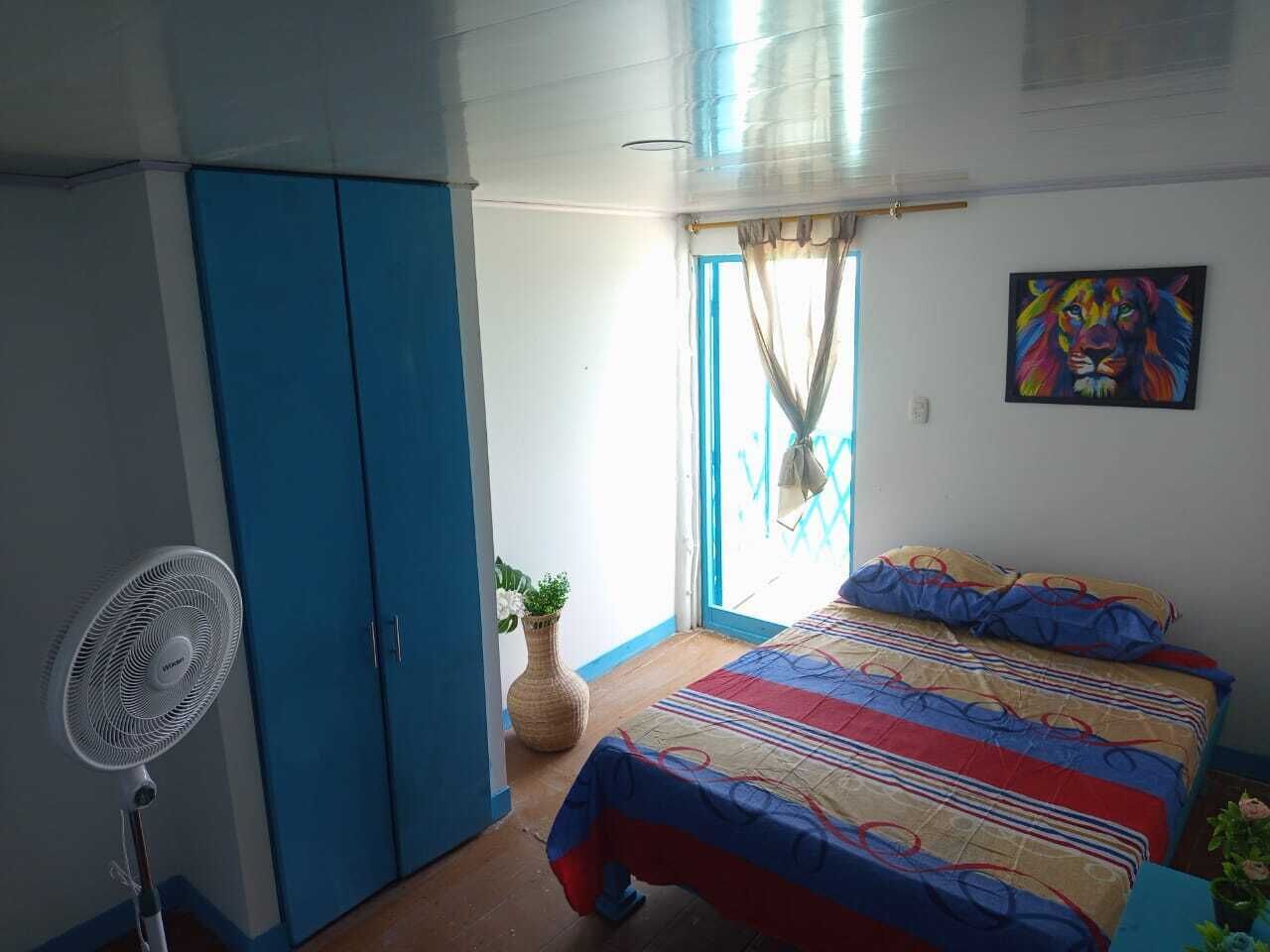 Een slaapkamer met een bed, een ventilator, een kledingkast en een raam met gordijnen.