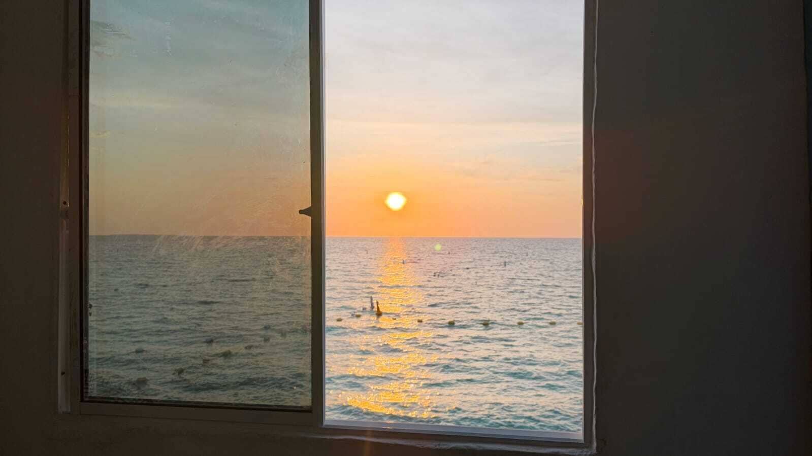 A window with a view of the ocean at sunset.