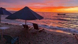 Ein Strand mit Sonnenschirmen, Liegen und einem Sonnenuntergang über dem Meer.