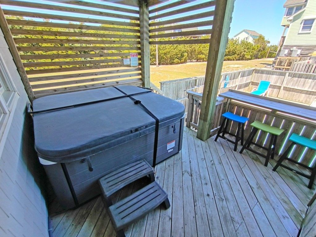 A covered outdoor deck with a hot tub, a barbecue grill, and a wooden fence.