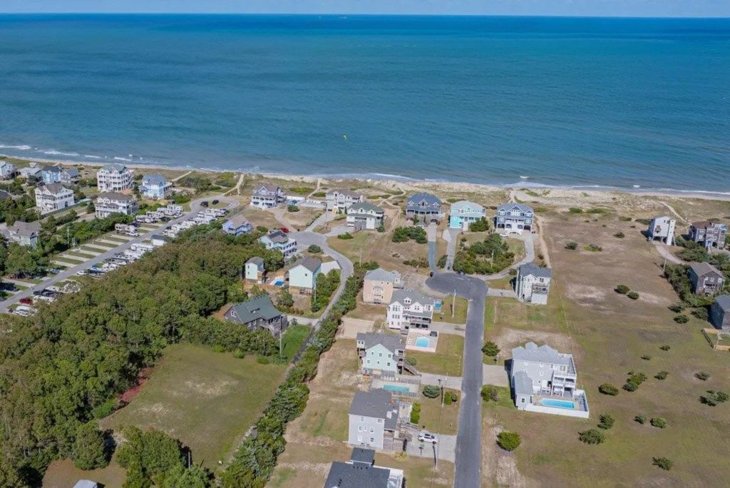 An aerial view of a coastal residential area with houses, a parking lot, and a beach.