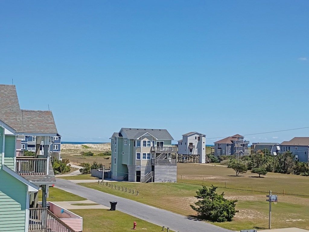 A coastal residential area with multiple houses, a clear sky, and a road leading to the beach.