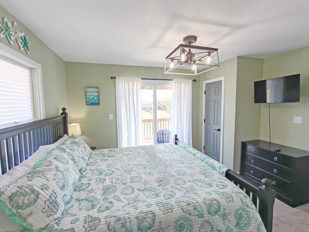 Un dormitorio con cama, cómoda, televisor y ventana con cortinas.