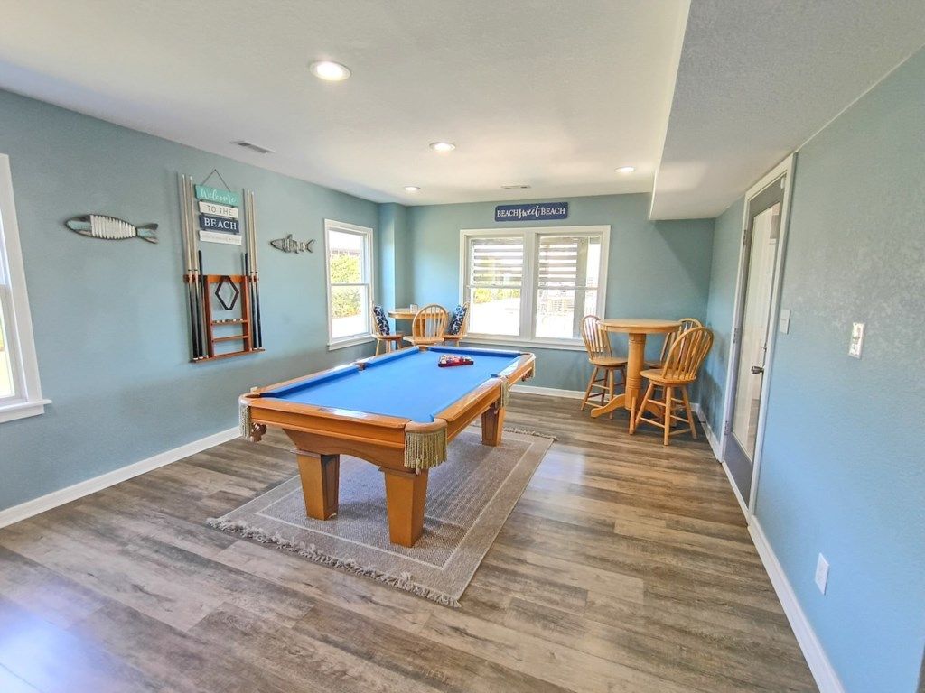 A pool table in a room with light blue walls, a wooden floor, and a window with blinds.