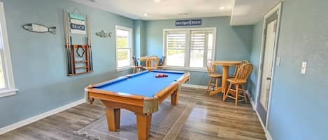 A pool table in a room with light blue walls, a wooden floor, and a window with blinds.