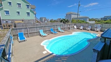 A swimming pool with lounge chairs, a wooden fence, and houses in the background.