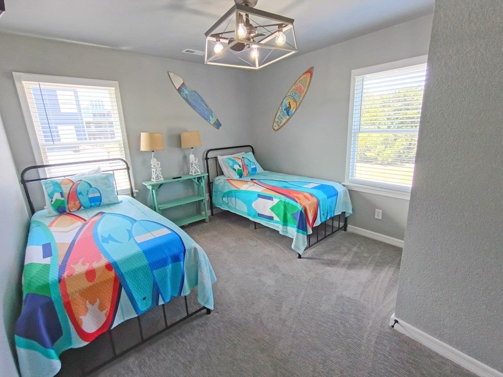A bedroom with two beds, a ceiling fan, and surfboards on the wall.