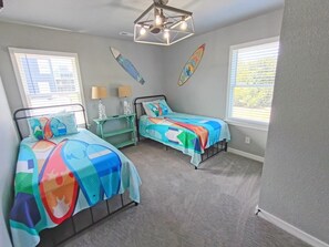 Quarto com duas camas, um ventilador de teto e pranchas de surf na parede.