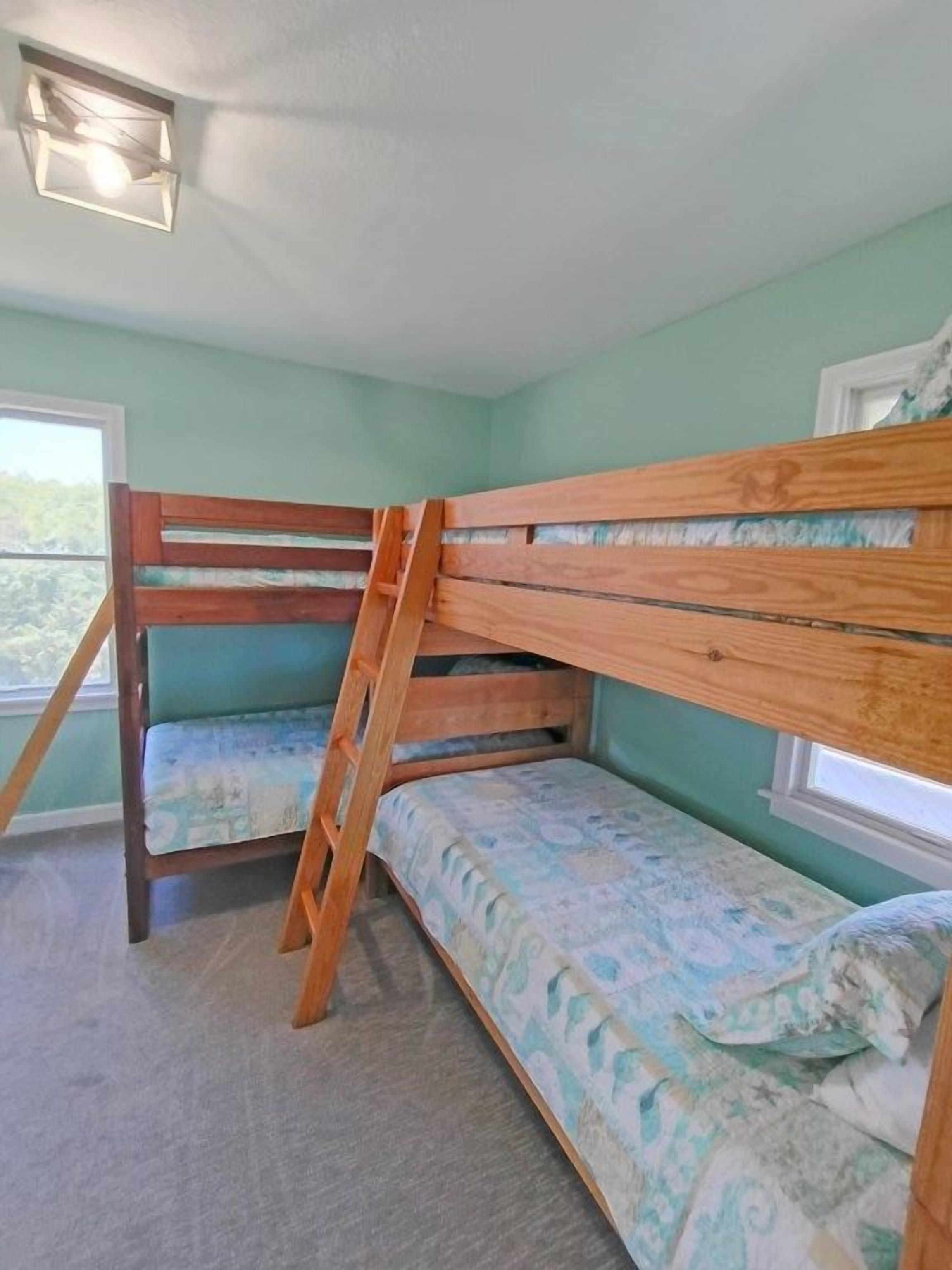 Une chambre avec un lit superposé, une fenêtre, un sol recouvert de moquette et une vue sur la verdure.