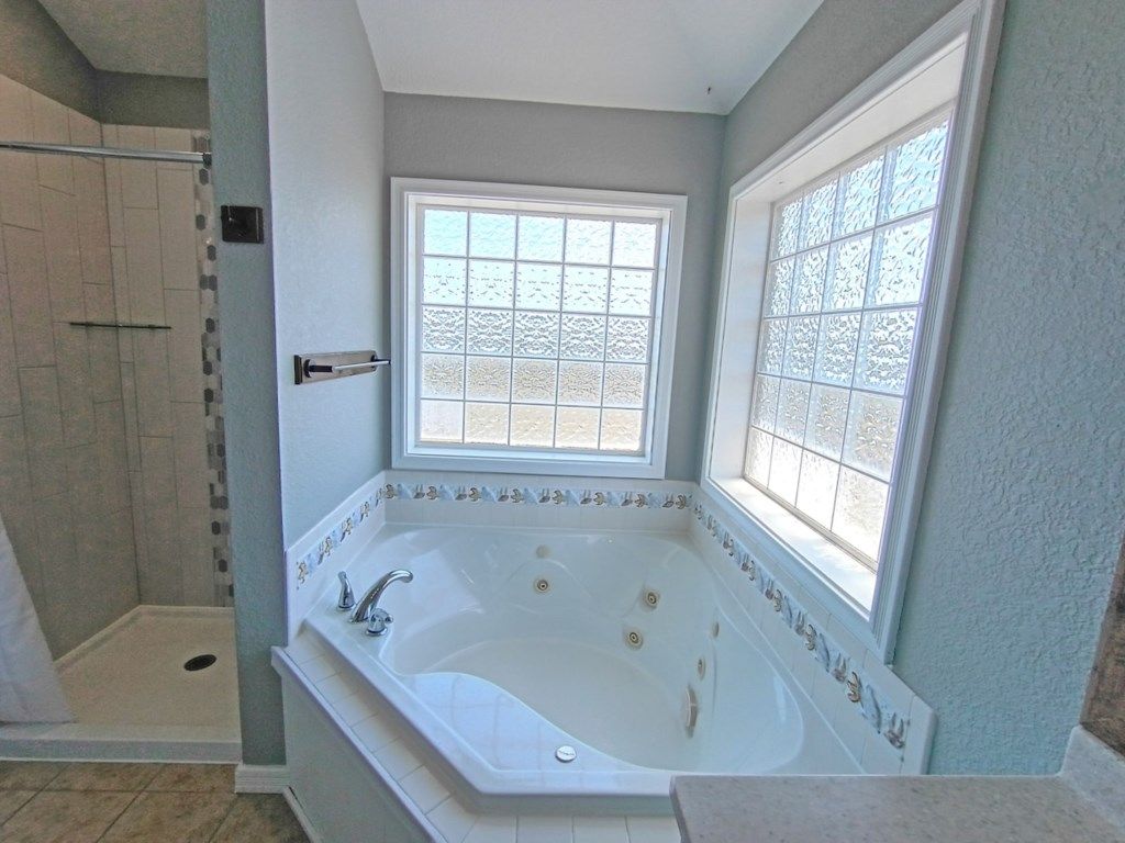 A bathroom with a large bathtub, a shower area, and a window with decorative glass.