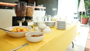 A breakfast buffet setup with bowls of fruit and cereal, a coffee dispenser, and stacked plates. - HOTEL MEDITERRANEO, located right in the heart of the city. Complimentary breakfast (Tulancingo)