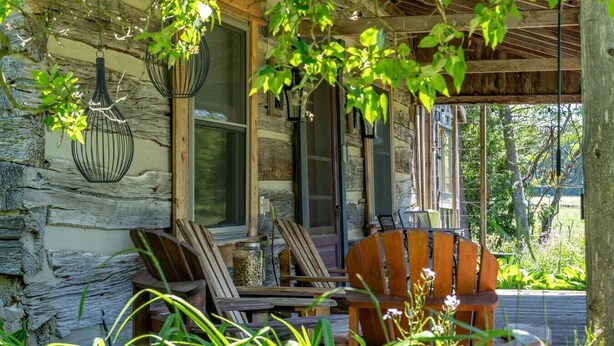 Eine rustikale Holzhütte mit Veranda, Holzstühlen und einer Steinmauer.