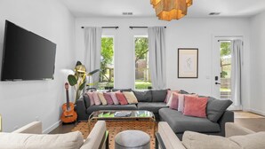 A modern living room with a sectional sofa, a coffee table, a flat-screen TV, and a guitar. - 8 Min to Broadway-Fenced Yard-Walkable East Nash (Nashville)