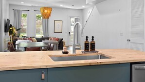 A modern kitchen with a wooden countertop, stainless steel sink, and a dining area with a sofa and table. - 8 Min to Broadway-Fenced Yard-Walkable East Nash (Nashville)