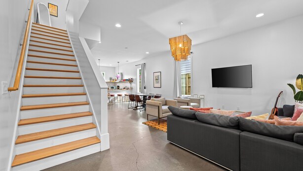 A modern interior with a staircase, a living area with a sofa, a dining area, and a TV mounted on the wall. - 8 Min to Broadway-Fenced Yard-Walkable East Nash (Nashville)