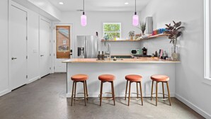 A modern kitchen with white cabinets, a central island with stools, pendant lights, and a window with a view. - 8 Min to Broadway-Fenced Yard-Walkable East Nash (Nashville)