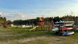 Une aire de jeux au bord du lac, avec des balançoires, un toboggan et un petit pavillon.