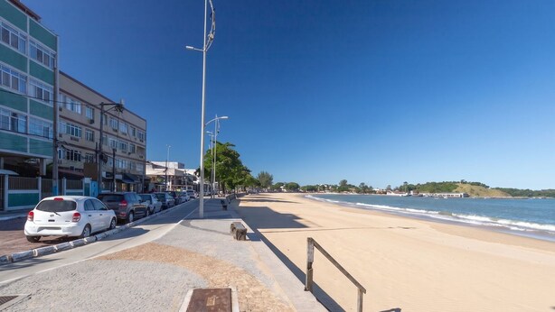 Una carretera costera con playa, coches aparcados y edificios.