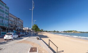 Una carretera costanera amb una platja, cotxes aparcats i edificis.