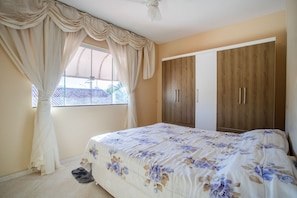 A bedroom with a bed, curtains, a wardrobe, and a window. - Apto com Garagem a 550 Metros da Praia do Centro (Rio das Ostras)