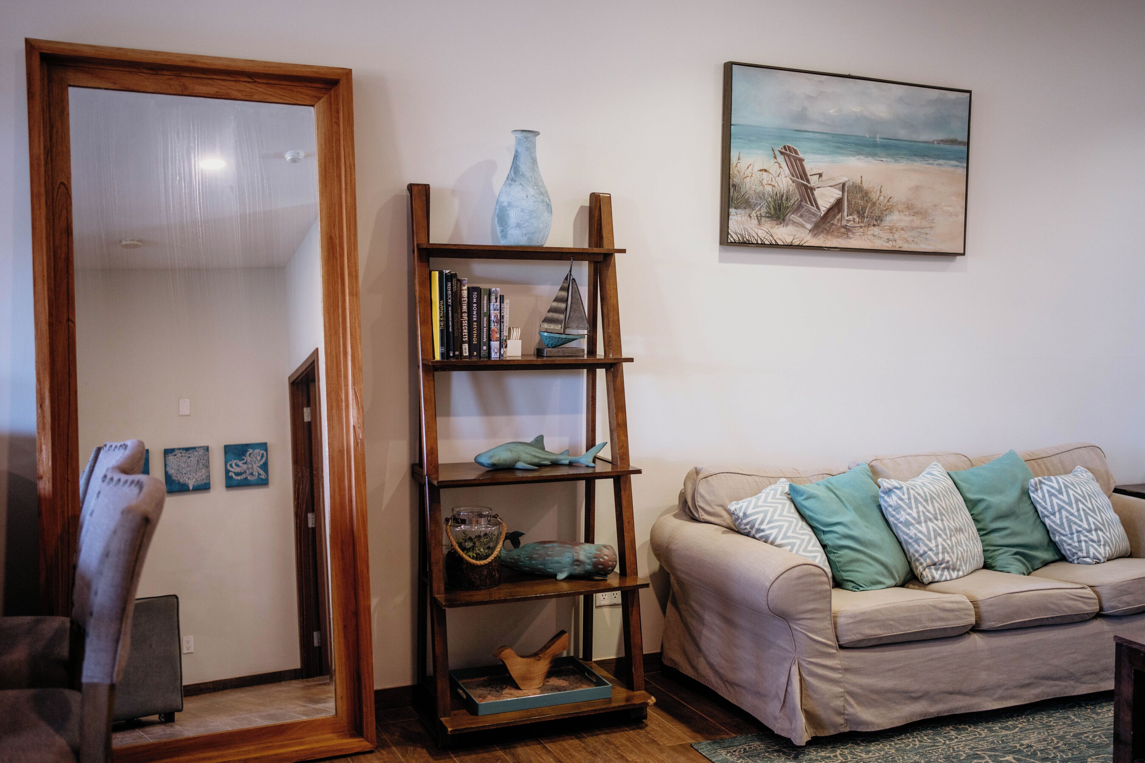 Un salon avec une bibliothèque en bois, un canapé beige orné de coussins à motifs, un tableau accroché au mur et une porte en bois.