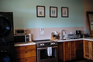 A kitchen with a washing machine, microwave, stove, sink, and wooden cabinets.