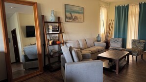 A living room with a sofa, armchair, coffee table, bookshelf, and a painting on the wall.